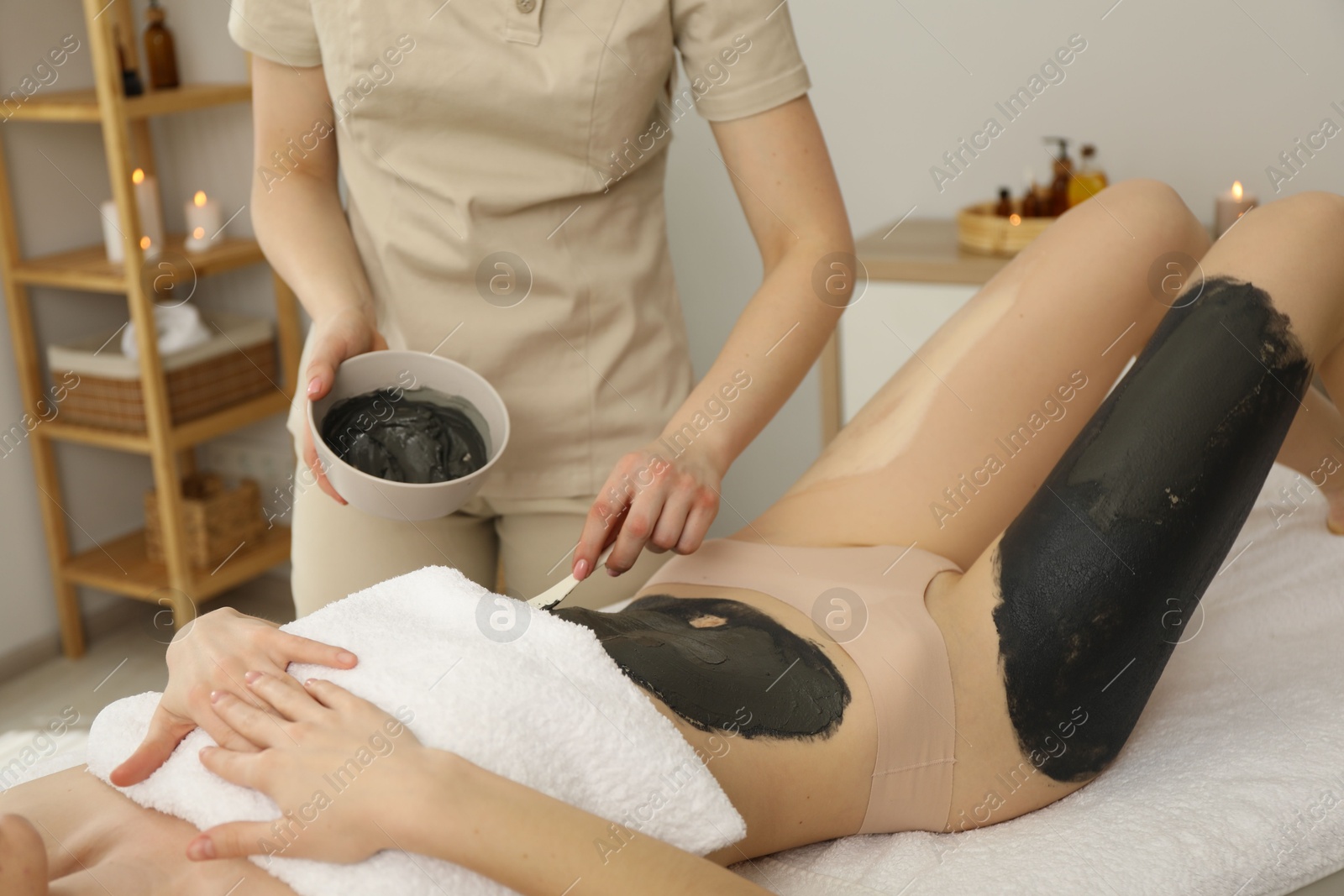 Photo of Esthetician applying cosmetic product for body wraps treatment onto woman's belly in spa salon, closeup