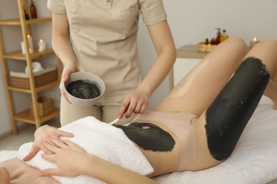 Esthetician applying cosmetic product for body wraps treatment onto woman's belly in spa salon, closeup