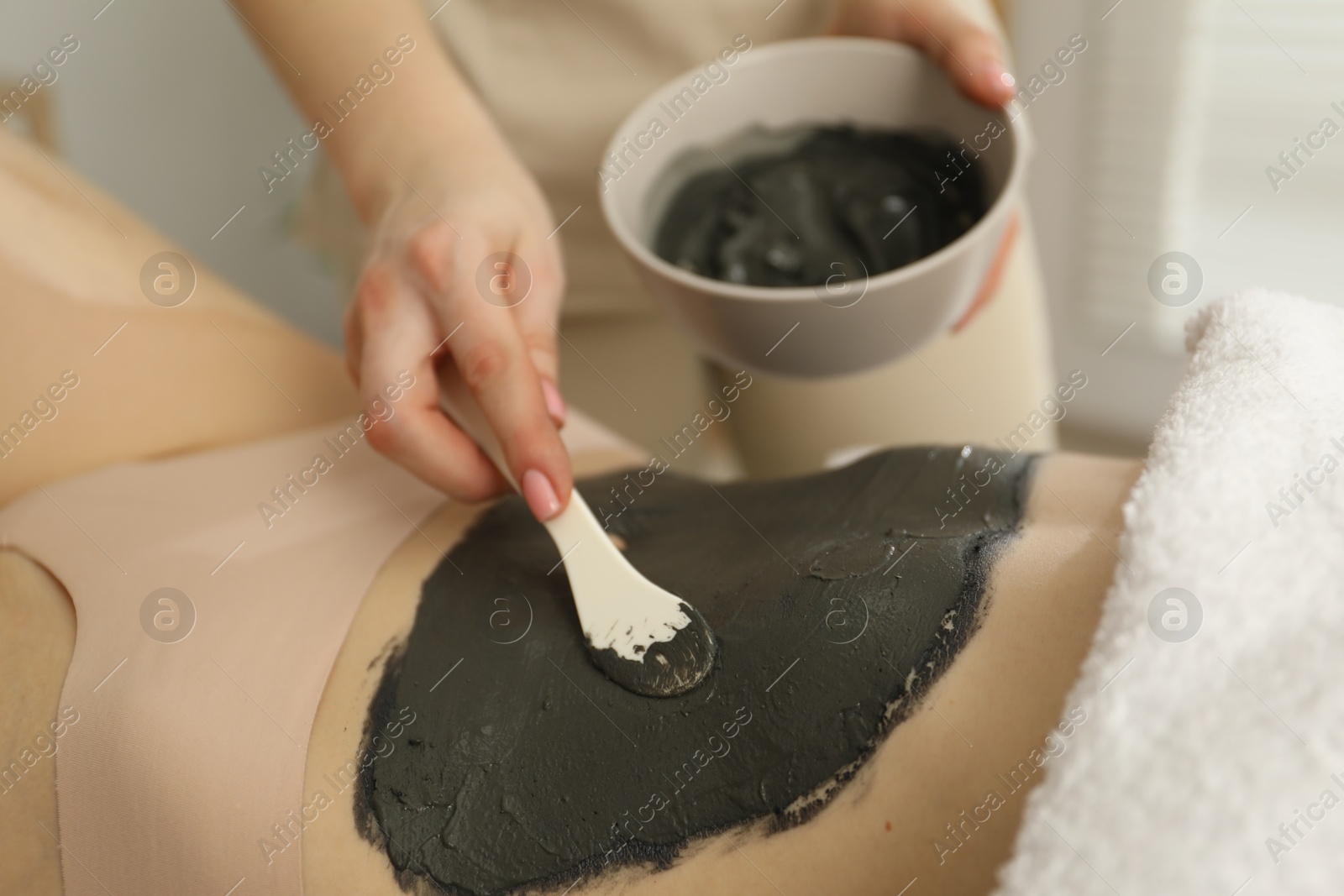 Photo of Esthetician applying cosmetic product for body wraps treatment onto woman's belly in spa salon, closeup