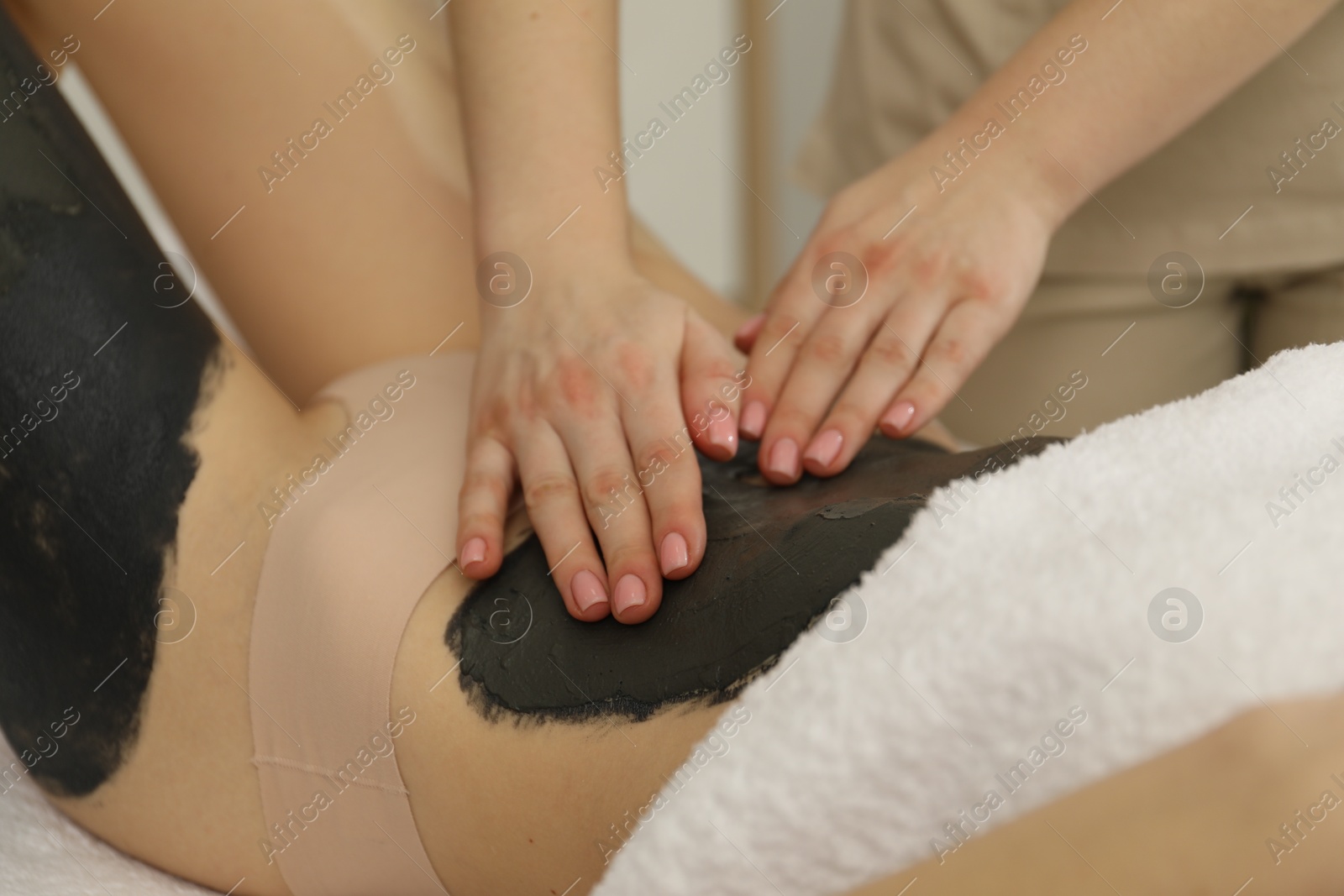 Photo of Esthetician applying cosmetic product for body wraps treatment onto woman's belly in spa salon, closeup