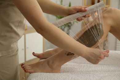 Photo of Woman undergoing body wraps treatment in spa salon, closeup