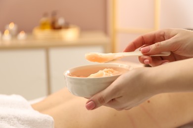 Photo of Esthetician applying cosmetic product for body wraps treatment onto woman's back in spa salon, closeup