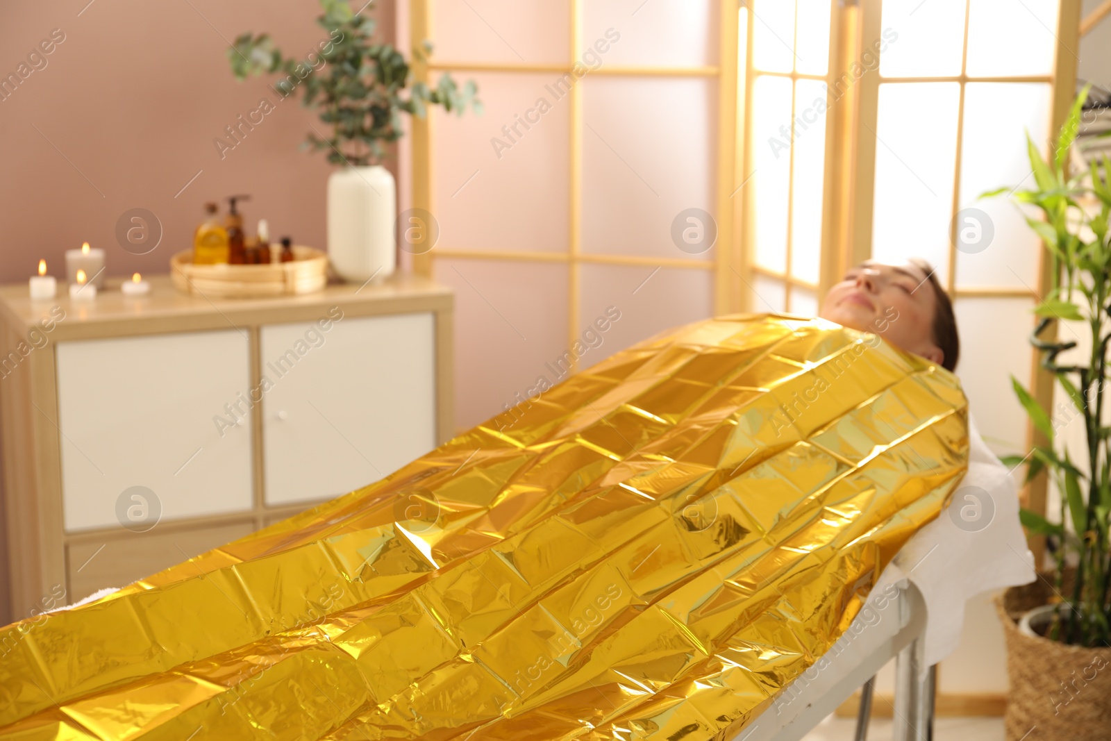 Photo of Woman covered with thermal foil blanket undergoing body wraps treatment in spa salon. Space for text