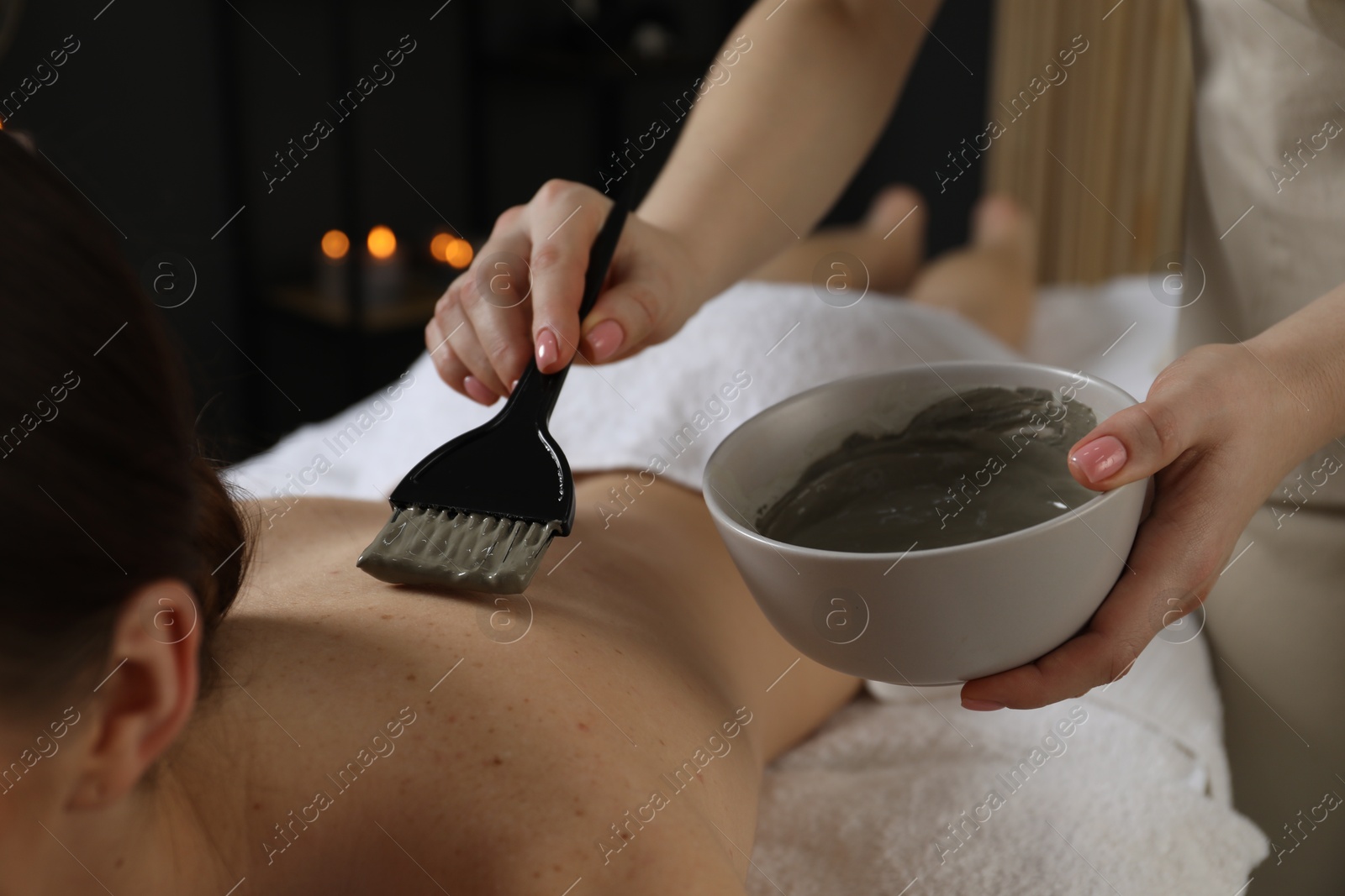 Photo of Esthetician applying cosmetic product for body wraps treatment onto woman's back in spa salon, closeup