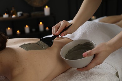 Photo of Esthetician applying cosmetic product for body wraps treatment onto woman's back in spa salon, closeup