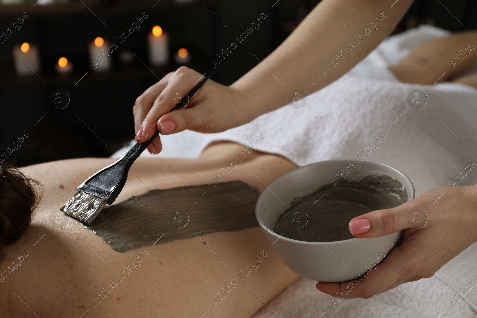 Photo of Esthetician applying cosmetic product for body wraps treatment onto woman's back in spa salon, closeup