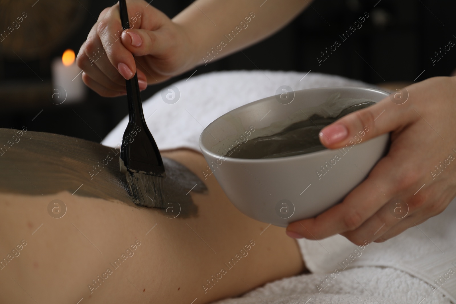 Photo of Esthetician applying cosmetic product for body wraps treatment onto woman's back in spa salon, closeup