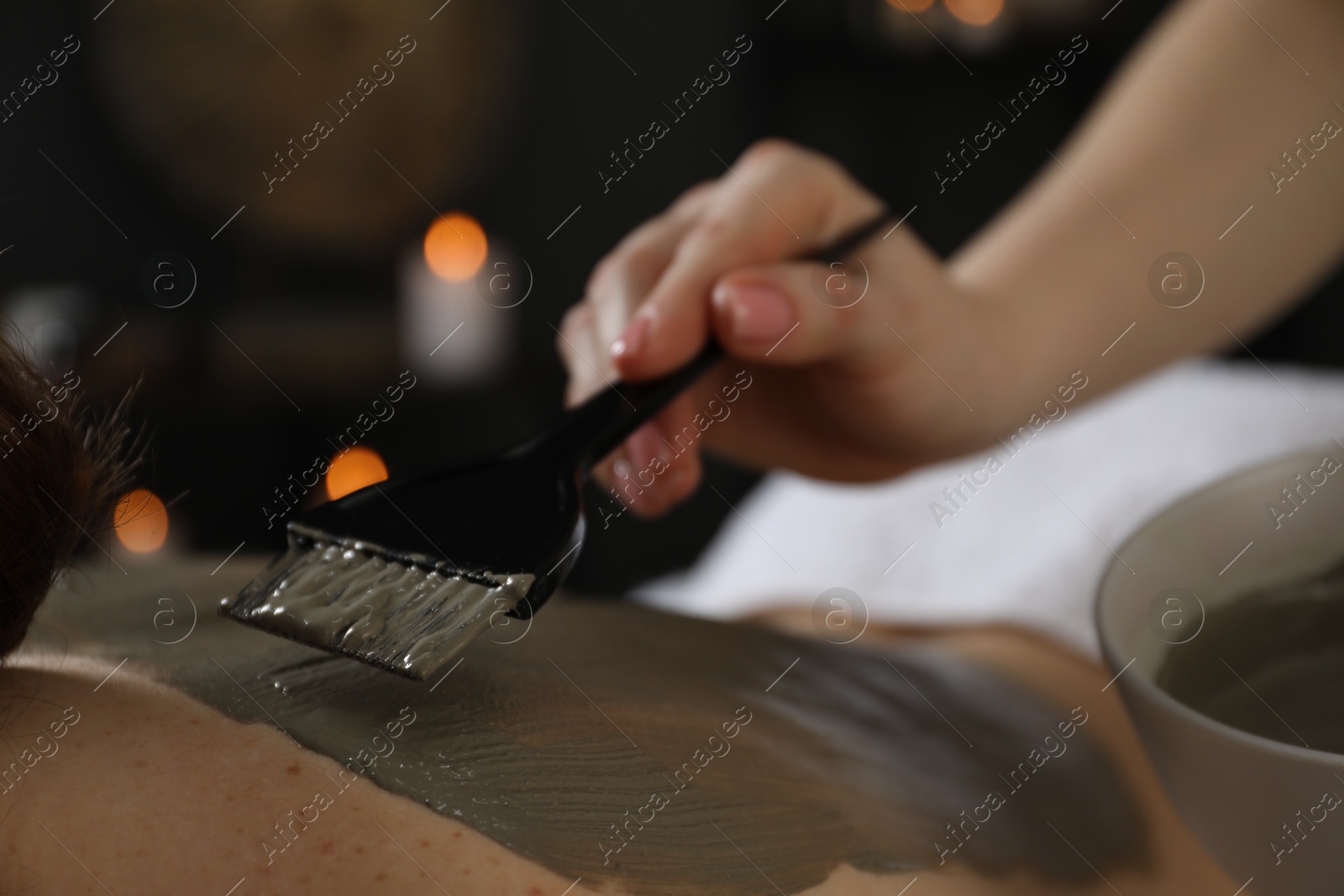 Photo of Esthetician applying cosmetic product for body wraps treatment onto woman's back in spa salon, closeup