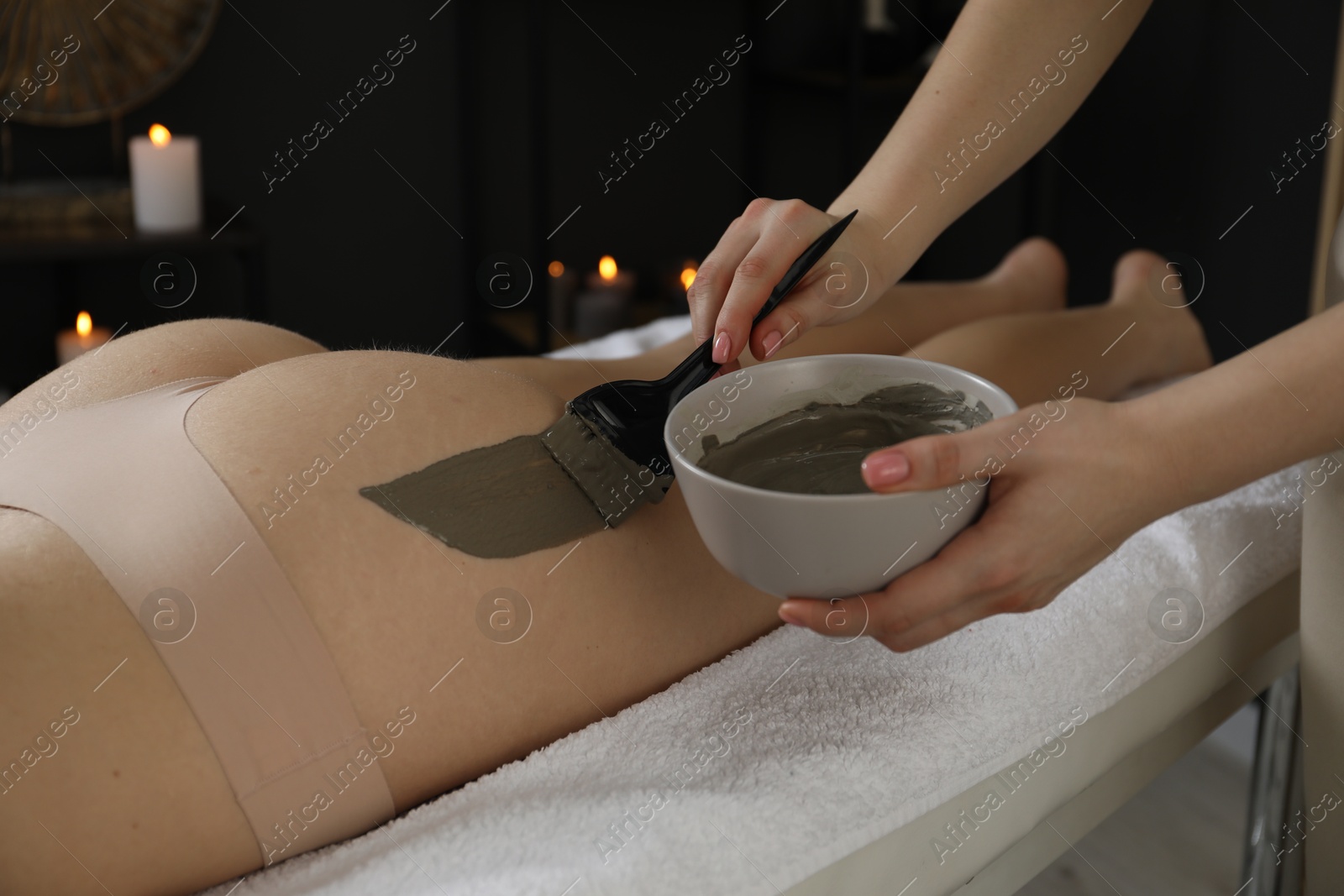 Photo of Esthetician applying cosmetic product for body wraps treatment onto woman's buttocks in spa salon, closeup