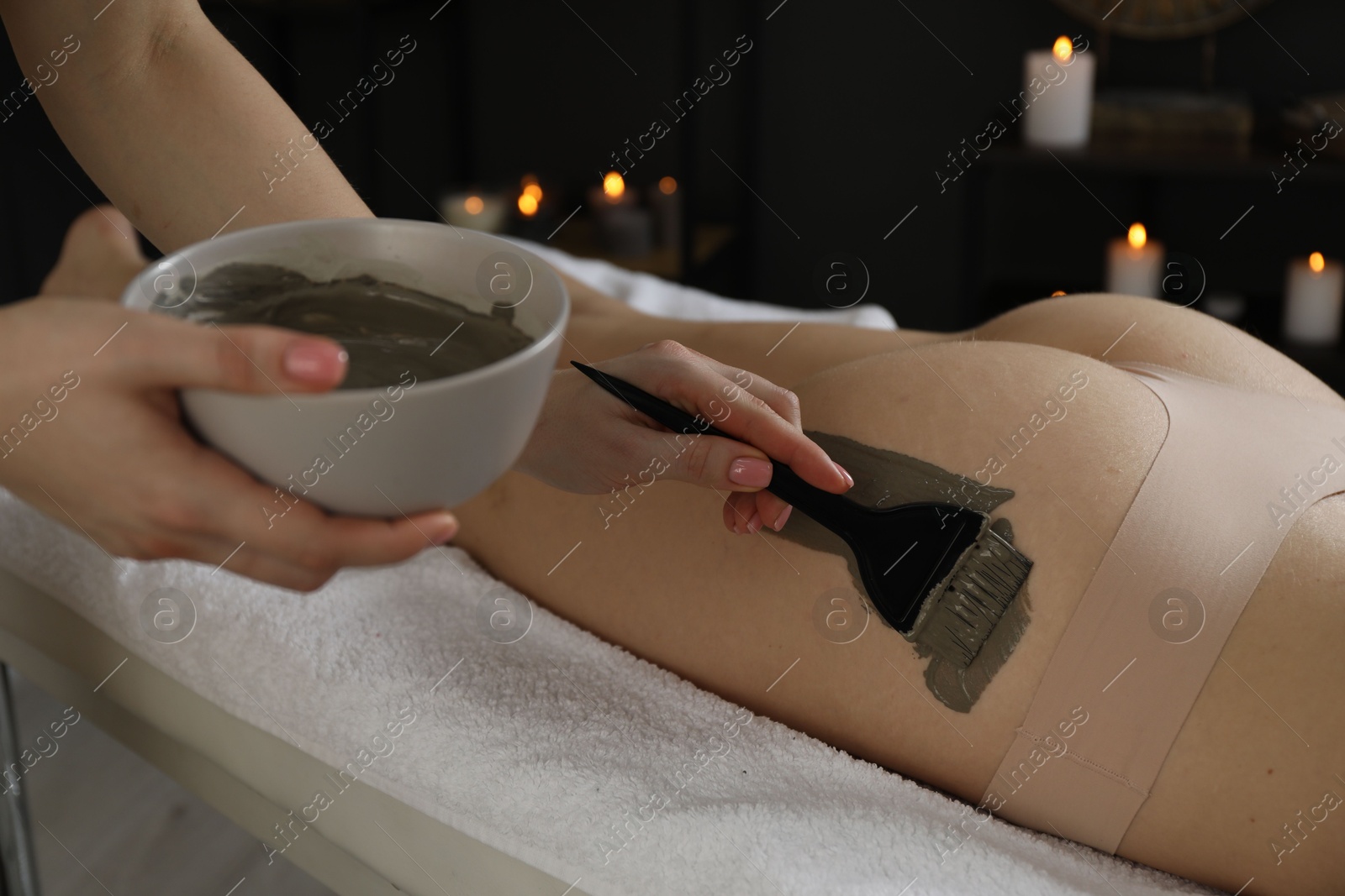 Photo of Esthetician applying cosmetic product for body wraps treatment onto woman's buttocks in spa salon, closeup