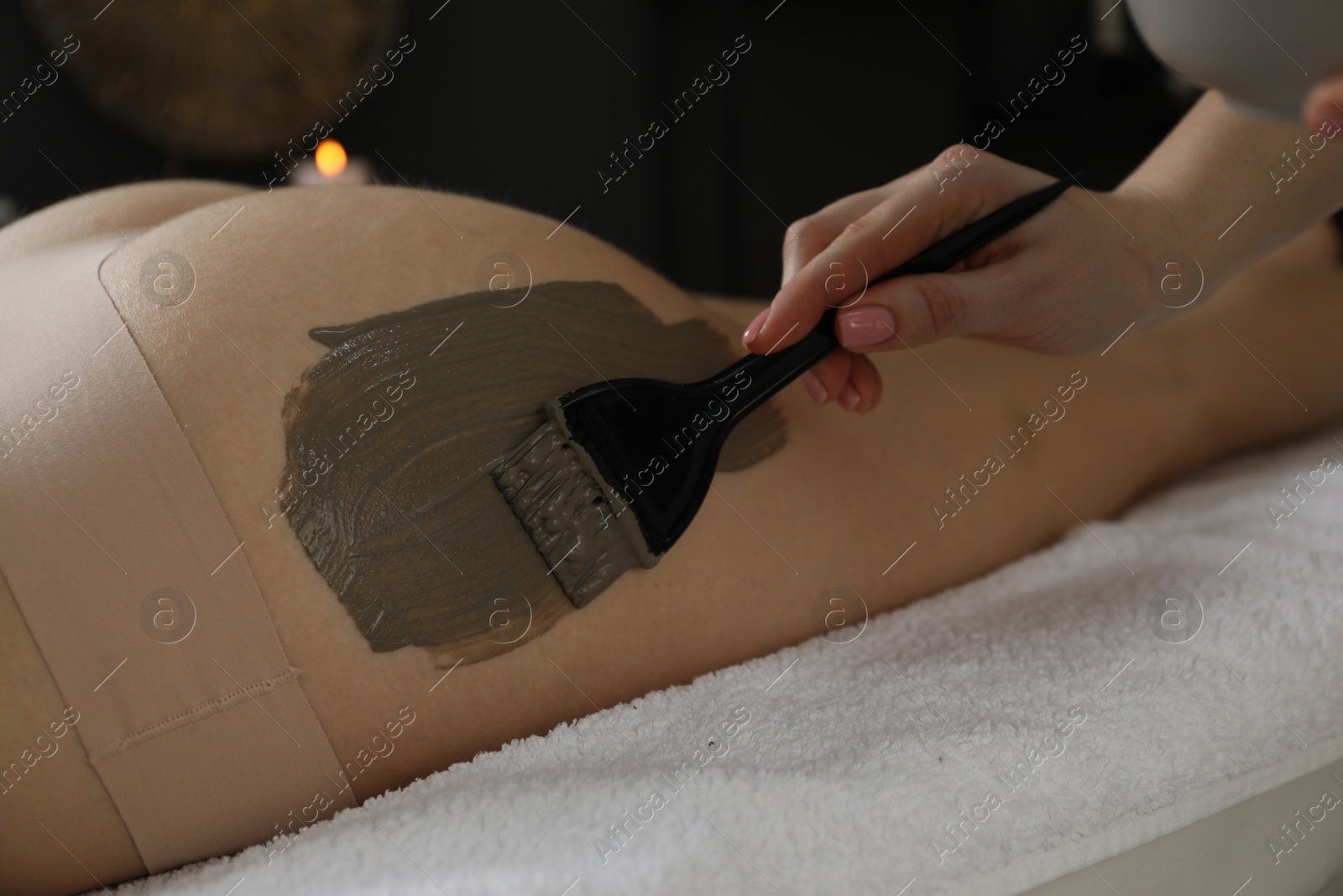 Photo of Esthetician applying cosmetic product for body wraps treatment onto woman's buttocks in spa salon, closeup