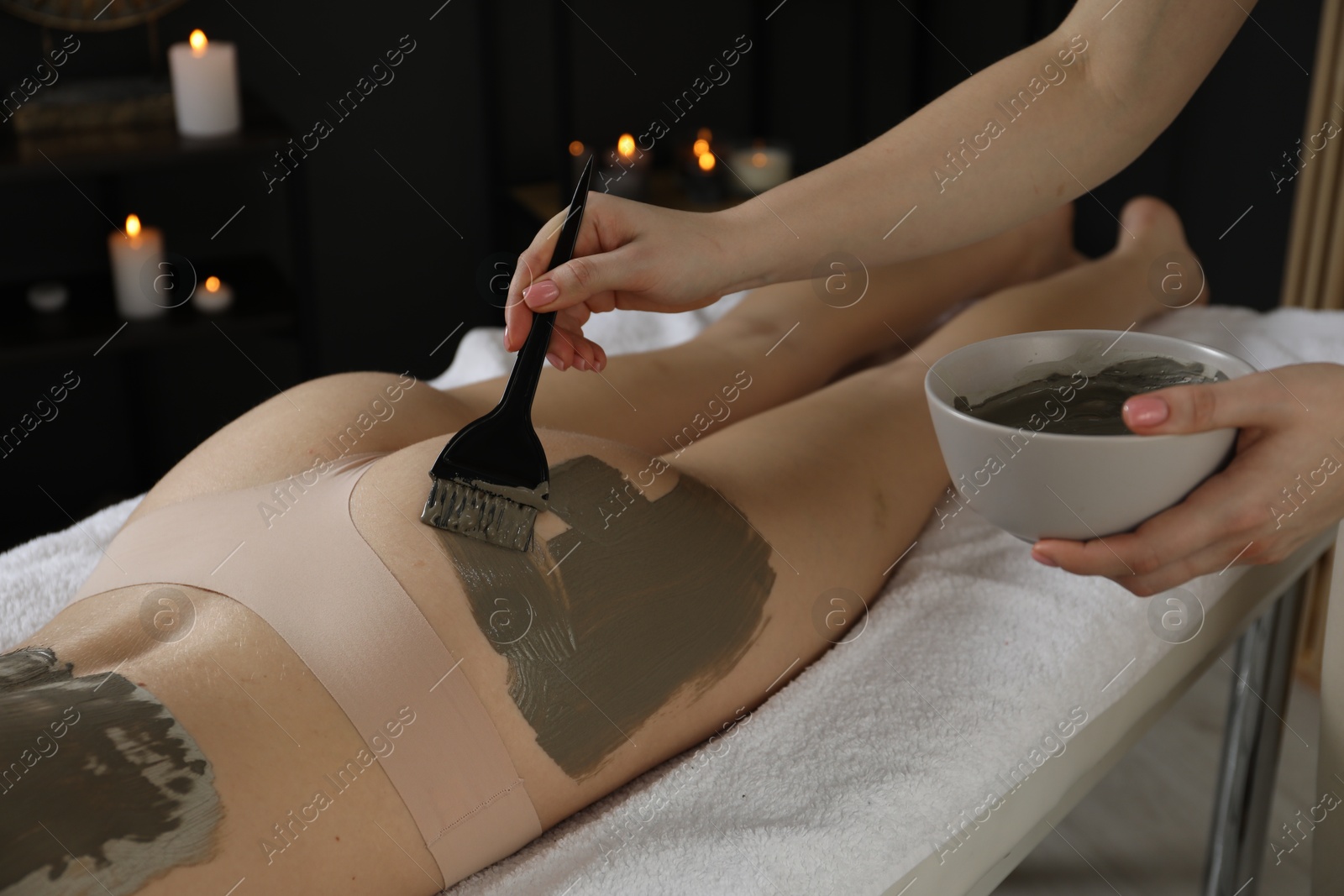 Photo of Esthetician applying cosmetic product for body wraps treatment onto woman's buttocks in spa salon, closeup