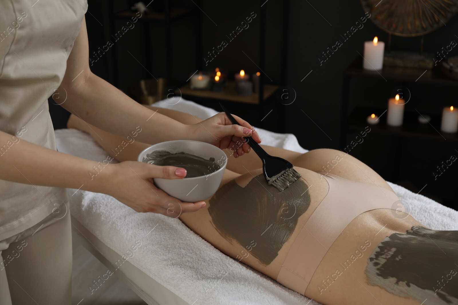 Photo of Esthetician applying cosmetic product for body wraps treatment onto woman's buttocks in spa salon, closeup