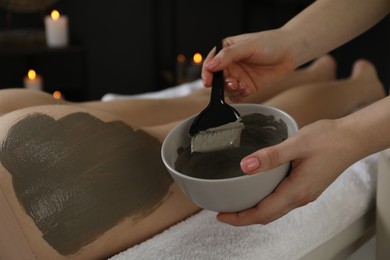 Photo of Esthetician applying cosmetic product for body wraps treatment onto woman's buttocks in spa salon, closeup