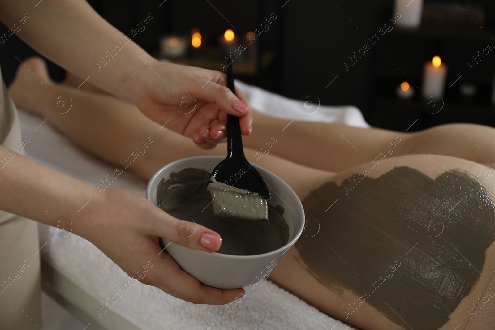 Photo of Esthetician applying cosmetic product for body wraps treatment onto woman's buttocks in spa salon, closeup