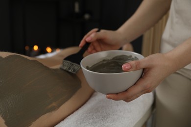 Photo of Esthetician applying cosmetic product for body wraps treatment onto woman's buttocks in spa salon, closeup