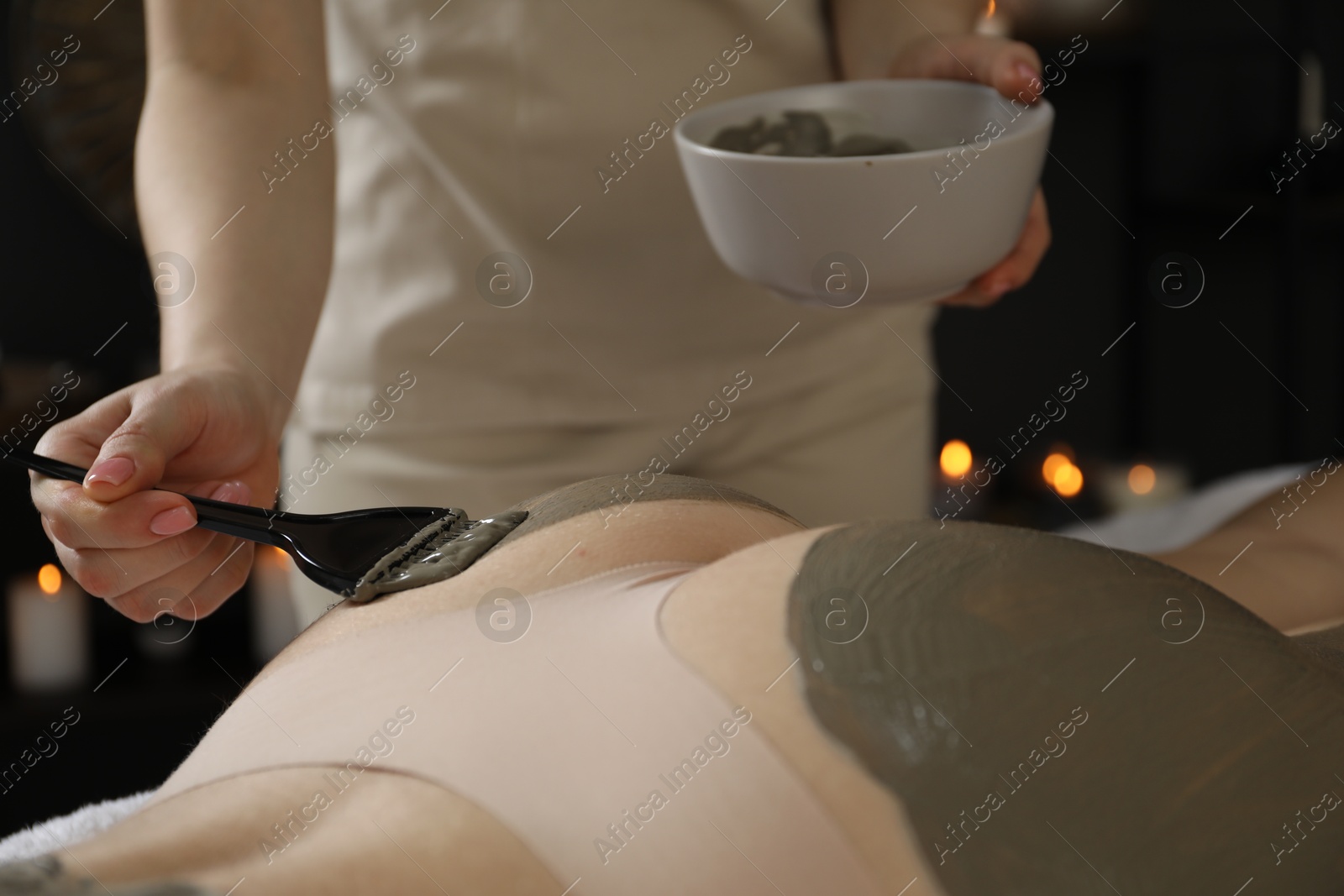 Photo of Esthetician applying cosmetic product for body wraps treatment onto woman's buttocks in spa salon, closeup