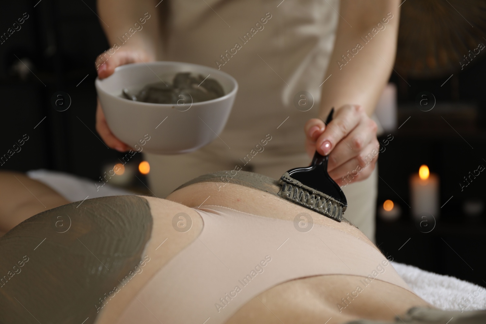 Photo of Esthetician applying cosmetic product for body wraps treatment onto woman's buttocks in spa salon, closeup