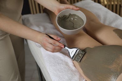 Photo of Esthetician applying cosmetic product for body wraps treatment onto woman's buttocks in spa salon, closeup