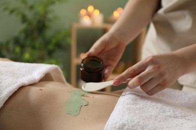 Photo of Esthetician applying cosmetic product for body wraps treatment onto woman's belly in spa salon, closeup