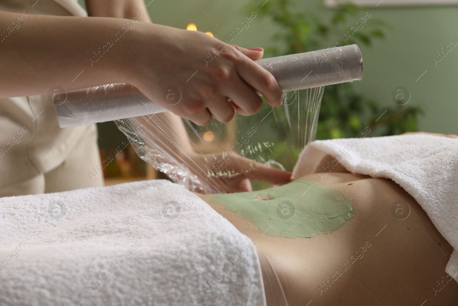 Photo of Woman undergoing body wraps treatment in spa salon, closeup