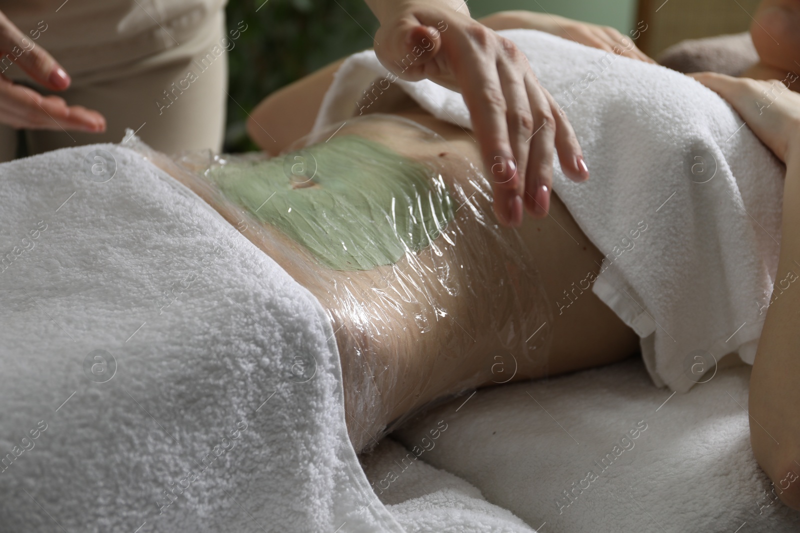 Photo of Woman undergoing body wraps treatment in spa salon, closeup