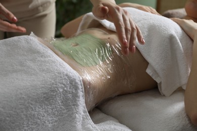 Photo of Woman undergoing body wraps treatment in spa salon, closeup