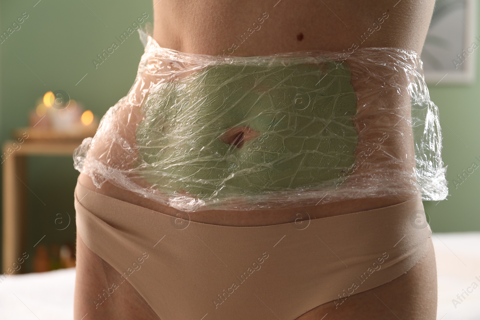 Photo of Woman doing spa body wraps on her belly in salon, closeup