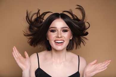 Portrait of beautiful young happy woman with gorgeous straight hair on dark beige background