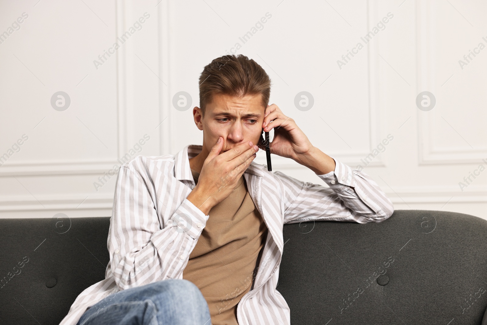 Photo of Worried man calling hotline for mental health help on sofa at home