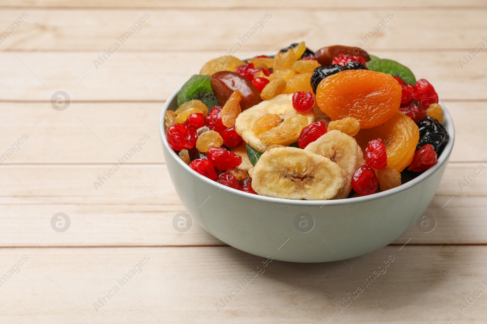 Photo of Mix of different dried fruits in bowl on wooden table, closeup. Space for text