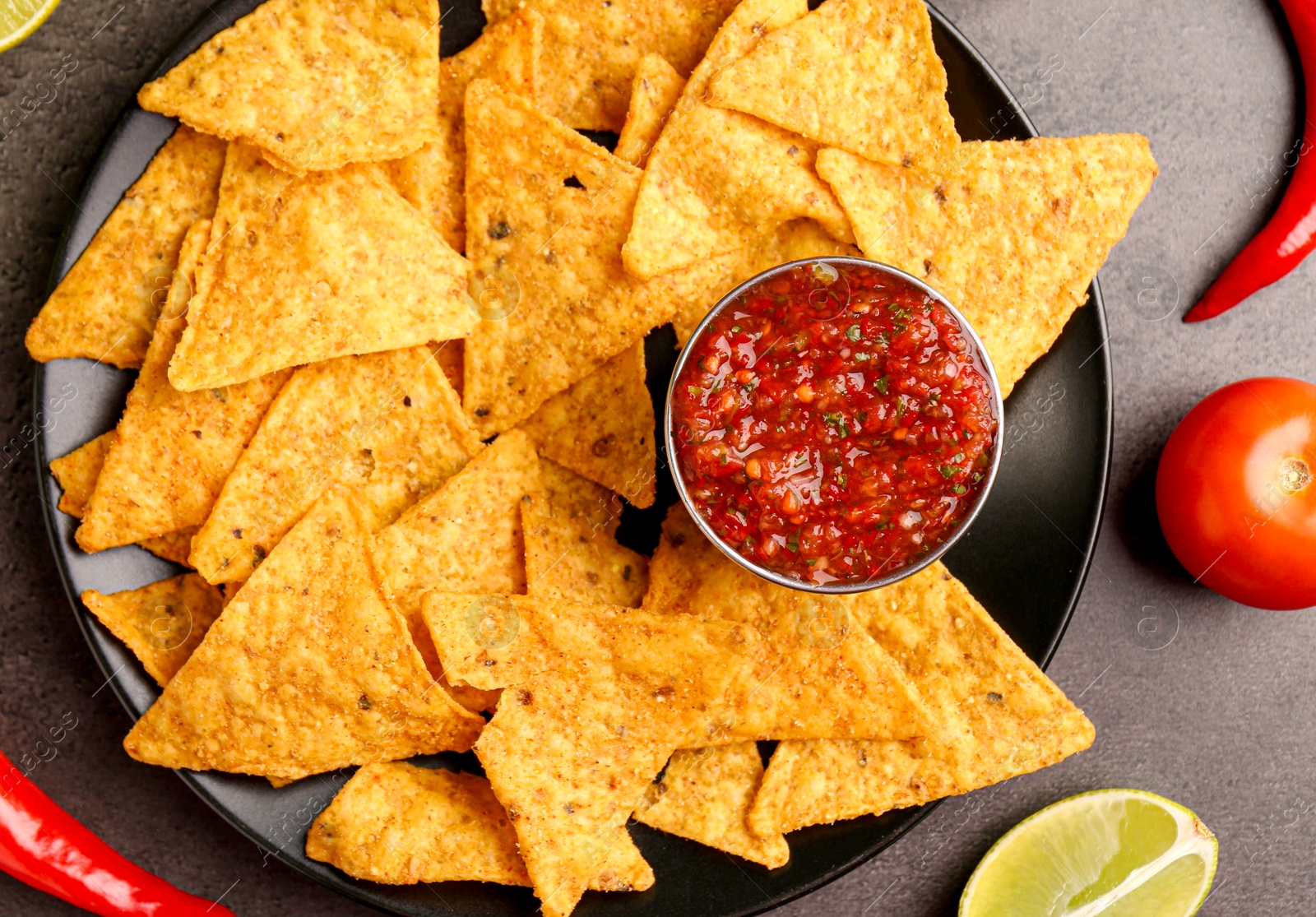 Photo of Delicious salsa sauce served with nachos and products on grey textured table, flat lay