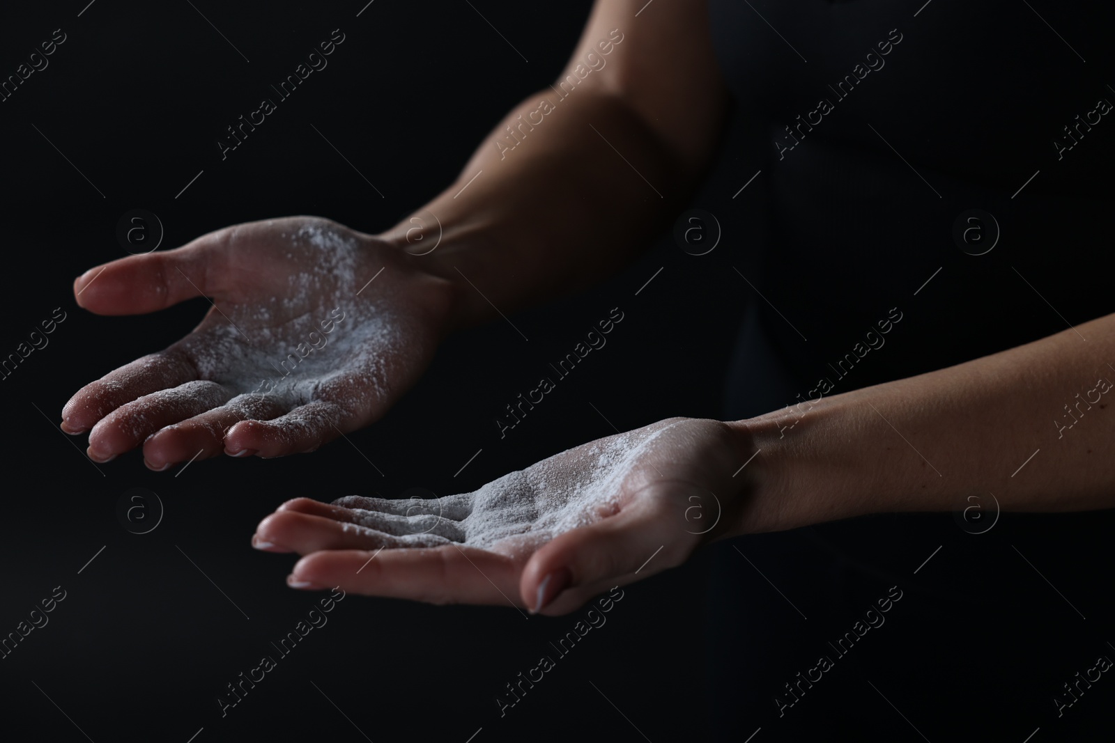 Photo of Woman with talcum powder on her hands before training against black background, closeup