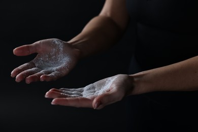 Woman with talcum powder on her hands before training against black background, closeup