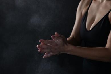 Woman clapping hands with talcum powder before training on black background, closeup. Space for text