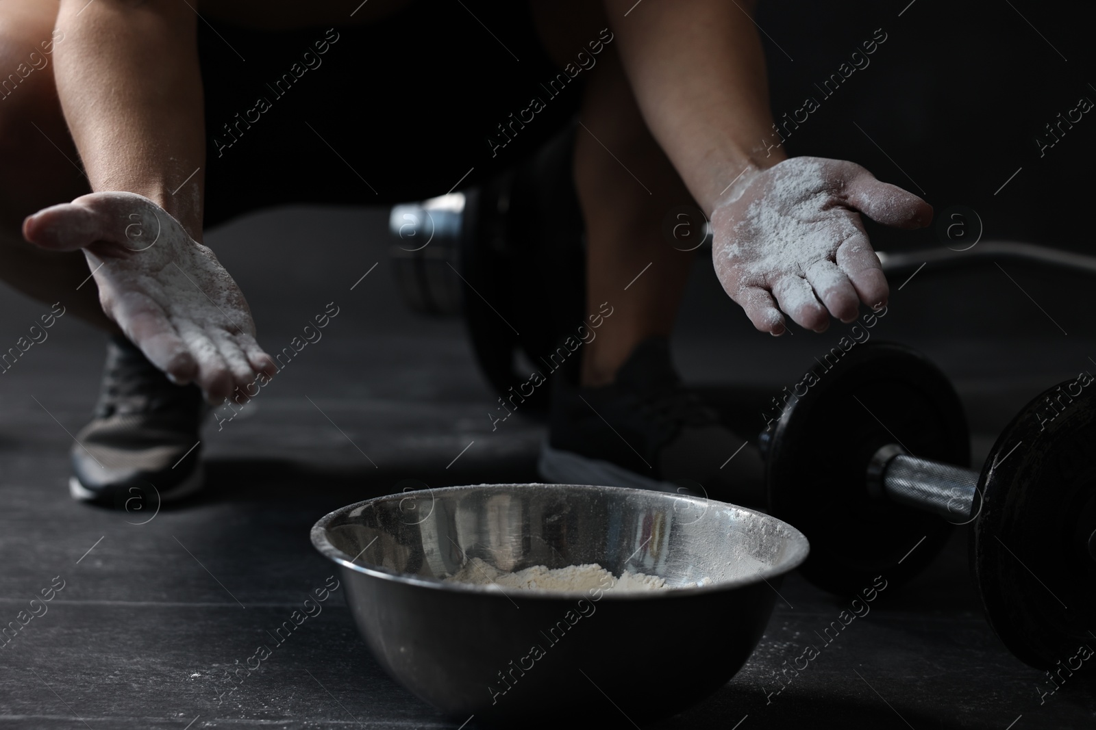 Photo of Woman applying talcum powder onto her hands above bowl before training in gym, closeup