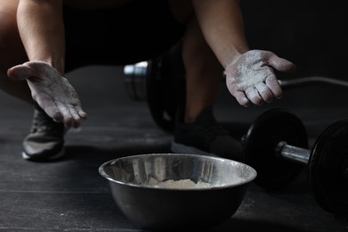 Woman applying talcum powder onto her hands above bowl before training in gym, closeup