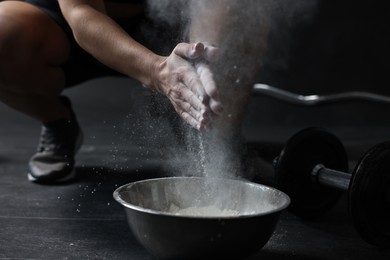 Woman clapping hands with talcum powder above bowl before training in gym, closeup