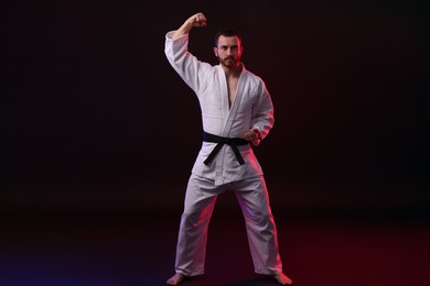 Photo of Man wearing uniform practicing karate in color lights against black background