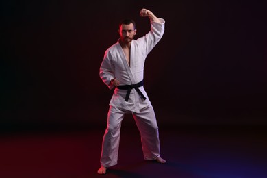 Photo of Man wearing uniform practicing karate in color lights against black background