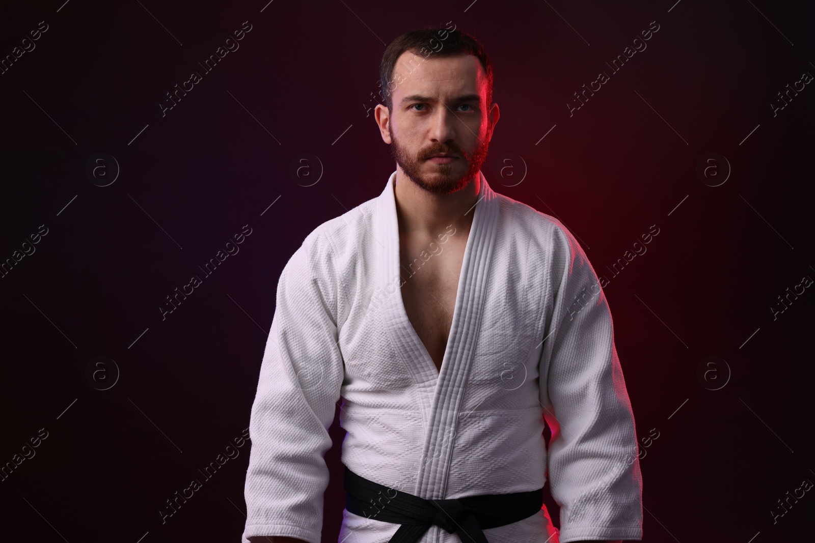 Photo of Karate fighter wearing uniform in color light against black background