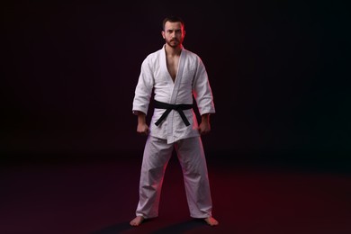 Photo of Karate fighter wearing uniform in color light against black background