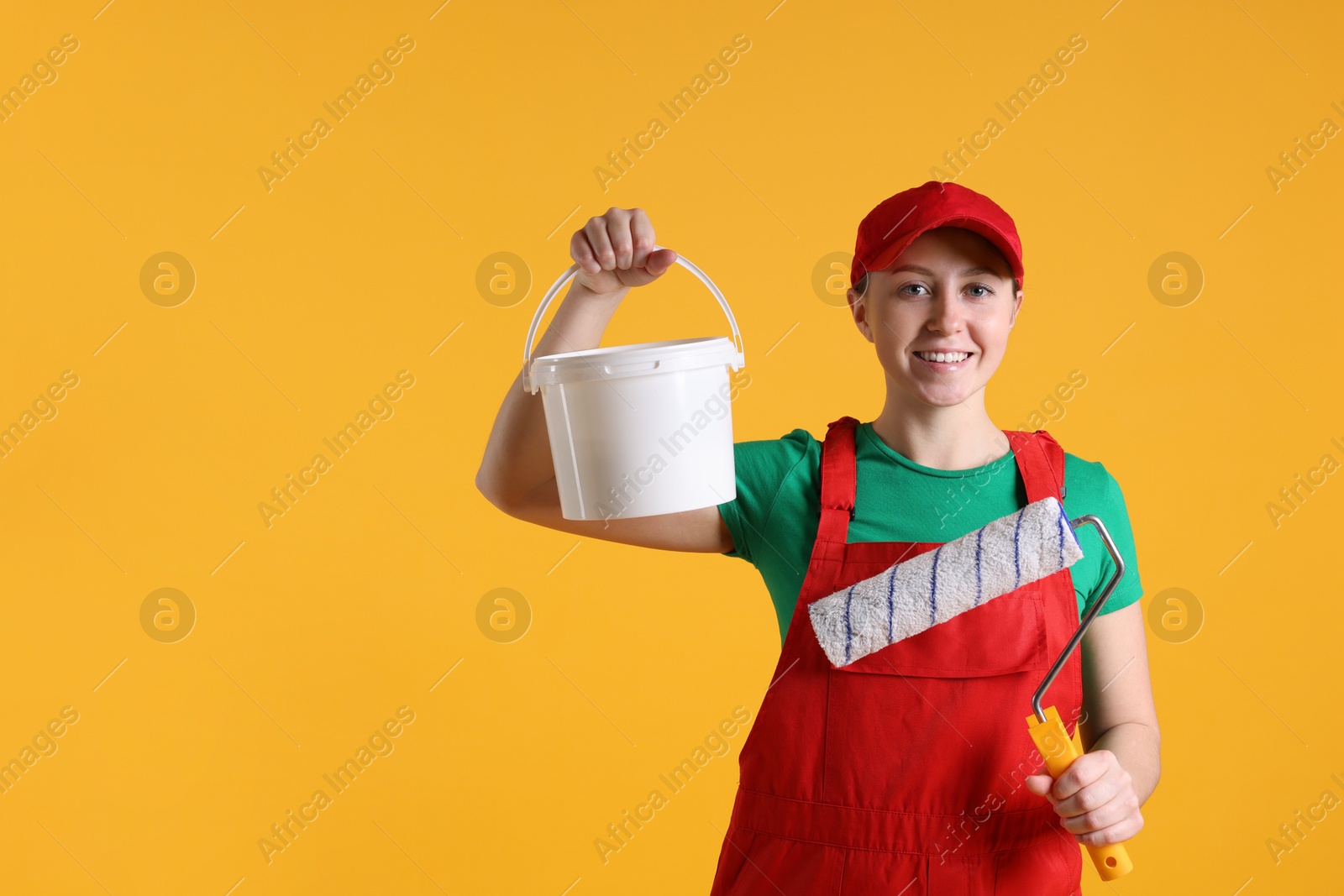 Photo of Professional painter with roller and bucket of paint on orange background. Space for text