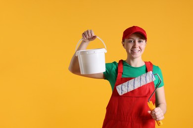 Photo of Professional painter with roller and bucket of paint on orange background. Space for text