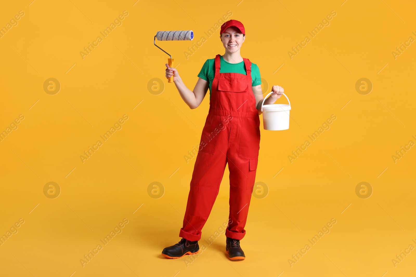 Photo of Professional painter with roller and bucket of paint on orange background