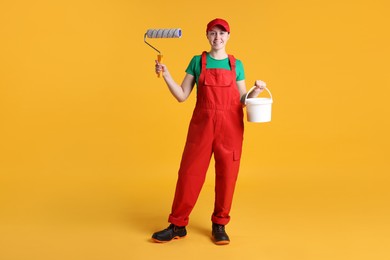 Photo of Professional painter with roller and bucket of paint on orange background