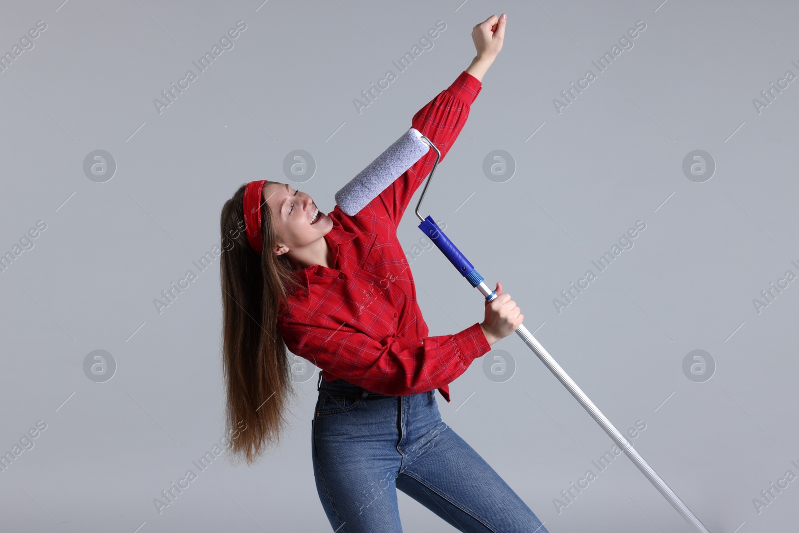 Photo of Woman with paint roller having fun on light grey background