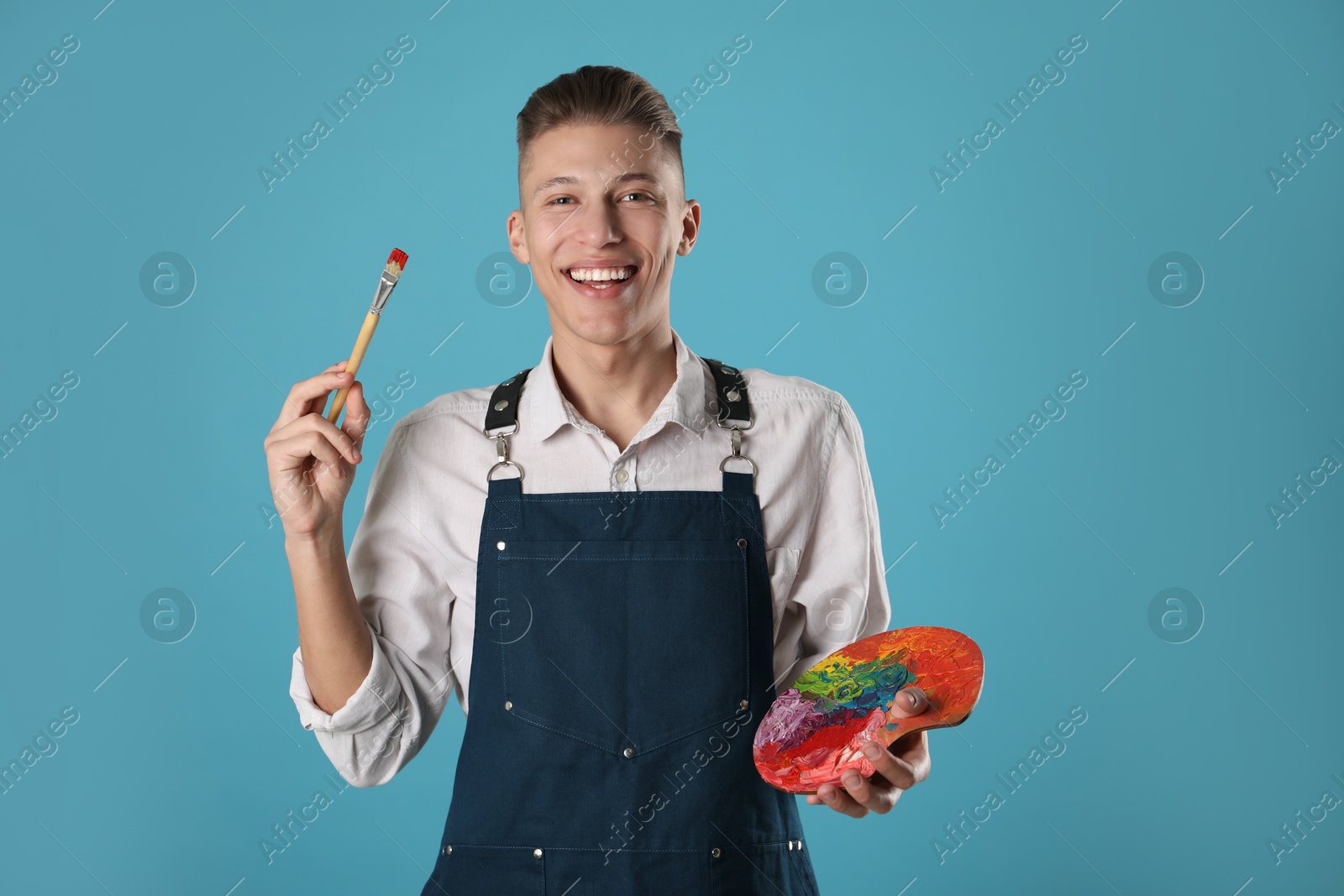 Photo of Smiling man with palette and paintbrush on light blue background