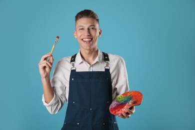 Smiling man with palette and paintbrush on light blue background