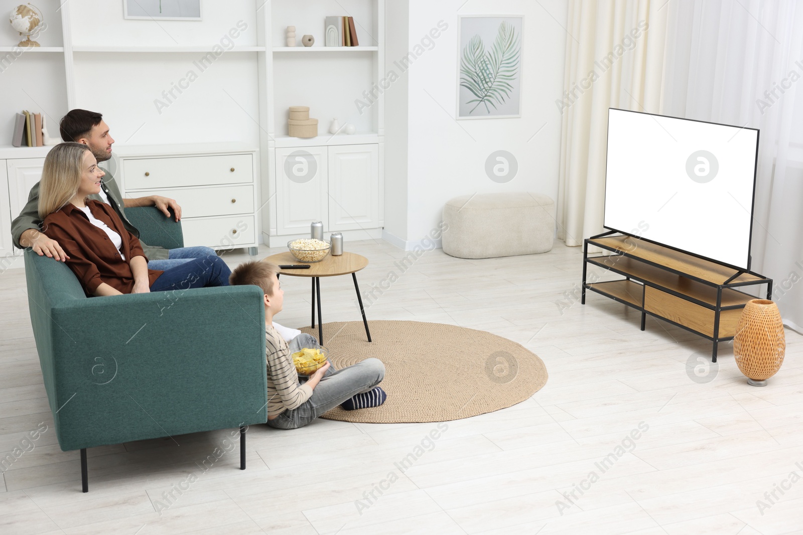 Photo of Happy family with snacks and drinks watching tv together at home